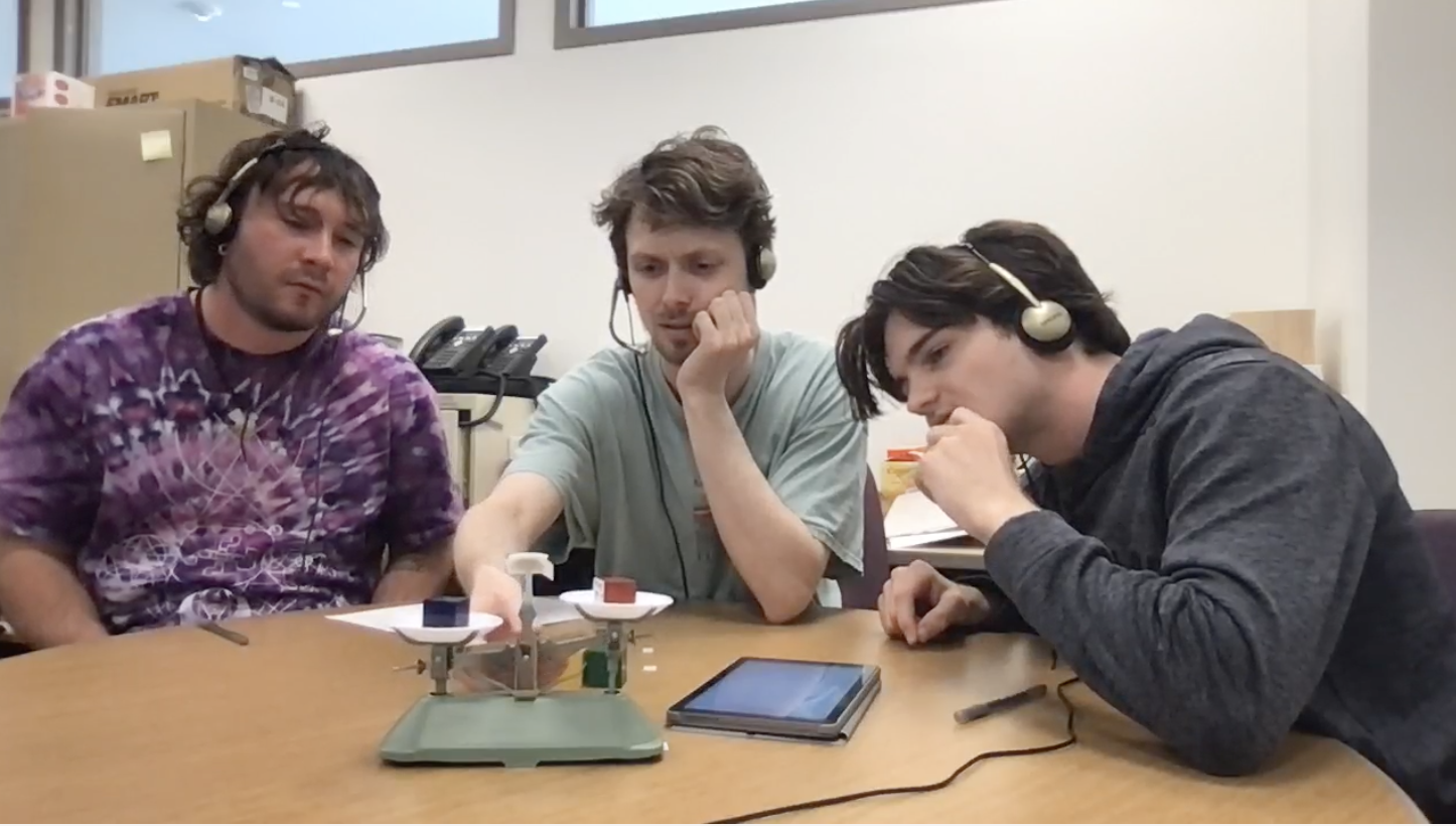 Three participants seated around a table wearing individual headphones and microphones, collaborating on the Weights Task problem-solving activity in a laboratory setting.